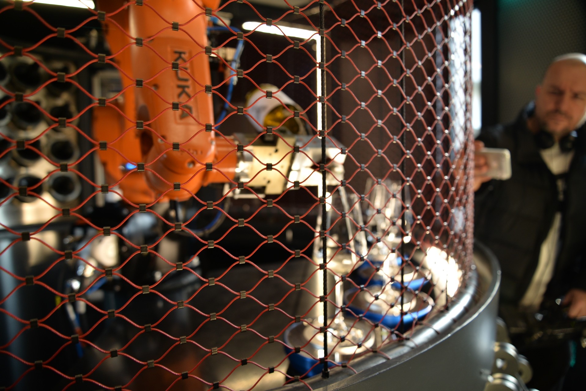 Robotická ruka v baru za bezpečnostní sítí dokáže nalít až 6 druhů vína. A když zrovna nemá co na práci, krátí si čas tancem robo barman